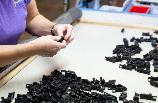 A worker sorts small black plastic parts on a table.