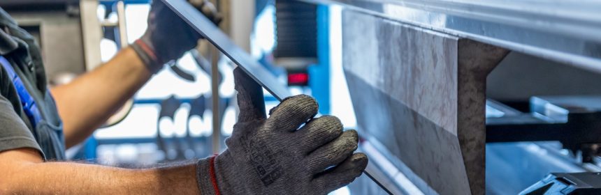 gloved employee inserting tube in tube bender in manufacturing facility