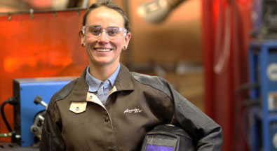 woman smiling with safety glasses holding welding helmet in plant