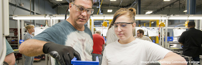 man and young woman wearing safety glasses and gloves inspecting product in manufacturing facility