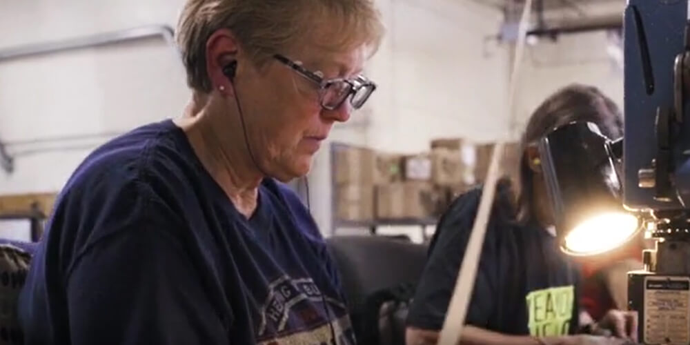 Two women are seated working on motor components in an industrial workshop.