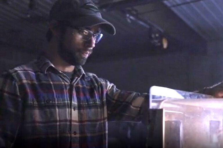 Young man in ball cap and safety glasses works at a grinding machine